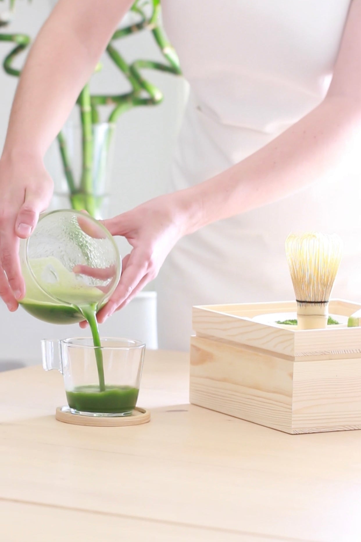 Pouring freshly prepared ceremonial matcha into a glass during a traditional matcha ritual. Traditional Japanese matcha preparation using a glass bowl and bamboo whisk